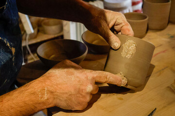 Potter's hand, the final touch as they shape and attach the handle to a cly mug
