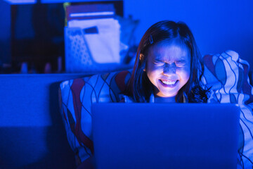 Asian girl sitting on the couch watching laptop at night. Parental control, screen addiction, and...