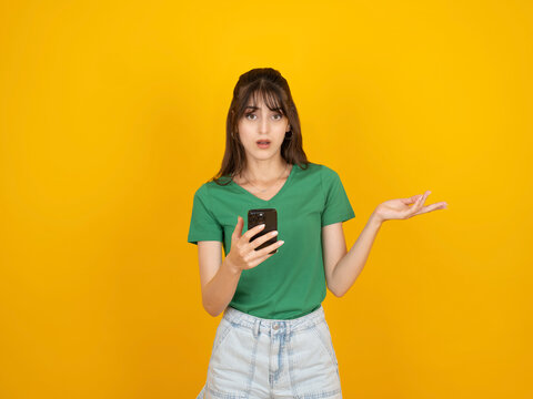 Unhappy woman using phone, photo of confused puzzled young caucasian unhappy woman using phone looking camera angry face emotion spread open hand asking questions isolated on yellow background.