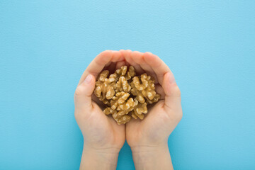 Little child boy opened palms holding heap of brown walnuts on light blue table background. Pastel color. Closeup. Point of view shot. Top down view.