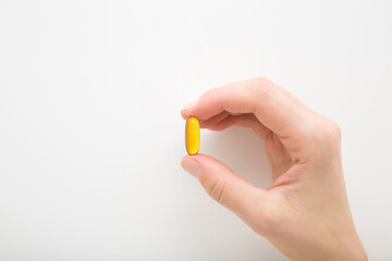 Young adult woman hand fingers holding and showing fish oil capsule or d vitamin on light gray...