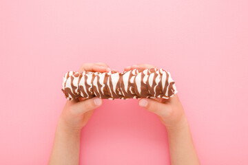 Little child girl hands holding and showing bar with white chocolate glaze and dark brown stripes on pink table background. Pastel color. Sweet snack. Closeup. Point of view shot. Top down view.