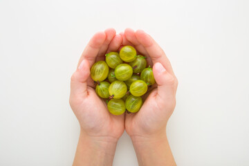 Little child girl opened palms holding and showing green gooseberries on light gray table background. Fresh berries. Closeup. Point of view shot. Top down view.
