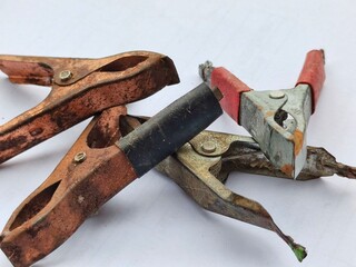 Close-up of old and rusty battery alligator clips on a white background, showing wear, corrosion, and signs of long-term use, ideal for industrial, electrical, or repair-themed concepts.