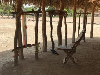 Wayuu weaving loom in Riohacha. Textile - making tools, craft heritage, thatched roof, wooden chair.