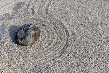Stone placed in raked gravel with curved lines in a dry landscape Japanese rock garden representing...