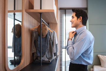 Get dress, asian young man, business man standing wearing shirt, female getting dressed preparing before go to work looking reflection in the mirror in the morning at home.