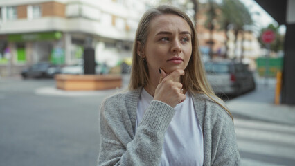 Fototapeta premium Woman standing on city street with thoughtful expression wearing casual attire while engaging with urban environment during daytime