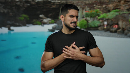 Young man at a resort poolside clutching his chest in discomfort, surrounded by lush outdoor hotel...
