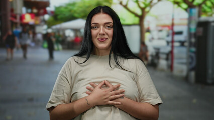 Woman smiling outdoors on a bustling city street with green trees in the background, embodying urban life and youthful energy in a casual beige outfit.