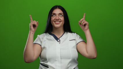 Woman smiling on isolated green background with curvy figure in casual clothing pointing upwards...