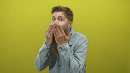 Man with ginger beard wearing denim jacket covers his mouth with both hands gesture in studio;...