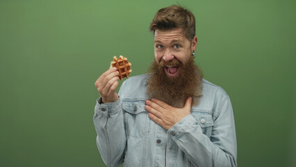 Man with long beard holding a waffle and placing hand on chest in green studio setting; delight surprise.