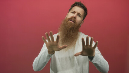 Man with long beard wearing white shirt pushes both palms forward toward camera in studio setting;...