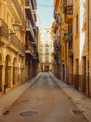 Historic Carrer de les Cuines in Ciutat Vella, Valencia, Spain, with sunlit balconies, wrought iron...
