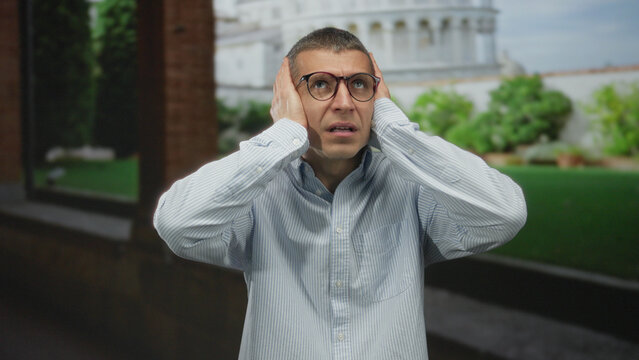 Fototapeta Man standing outdoors near pisa tower with a shocked expression, wearing glasses and a striped shirt, in a picturesque italian street setting during the day.