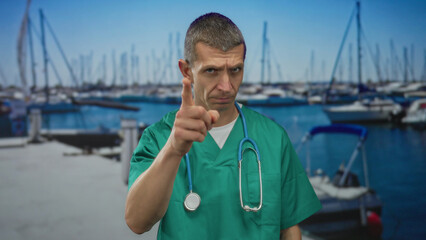 Caucasian male doctor with stethoscope wearing uniform points finger at camera by the seaside port...
