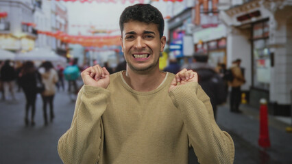 Obraz premium Man shows hands raising concern on street as young hispanic male stands in outdoor road public area.