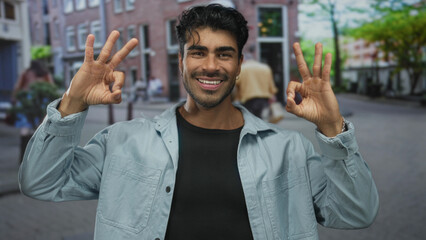 Man holds hand in ok sign while smiling on street amid blurred pedestrians; approval confidence...