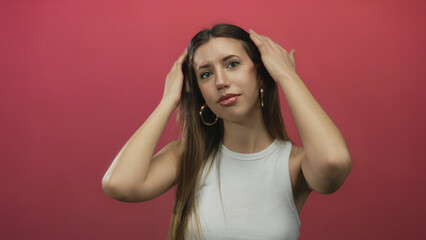 Fototapeta premium Woman touches hair and tilts head showing exposed shoulder in studio against pink wall; calm confidence.