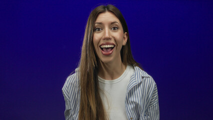Woman holds open hands gesture in blue studio setting with striped shirt and long hair framing her...
