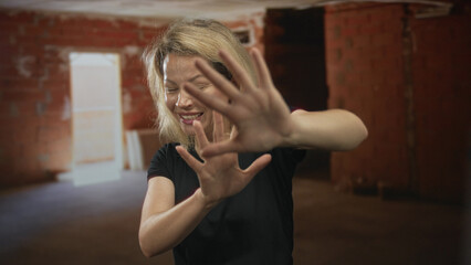 Young woman covers eyes and face with hands amid unfinished bare brick walls in a building...