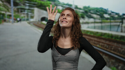 Woman at train station happily closing eyes with outdoor railway landscape in background, embodying young joy and travel anticipation.