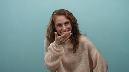 Woman laughing in a cozy sweater in front of a blue background, expressing joy and happiness.
