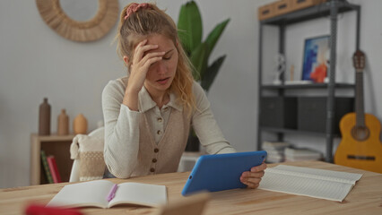 Woman holds tablet with anxious look at home and blonde young student pressing forehead over...
