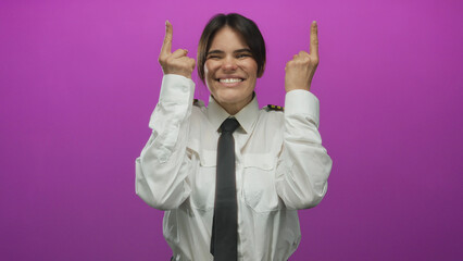 Young hispanic woman pilot in uniform pointing upwards against pink wall with a joyful expression,...