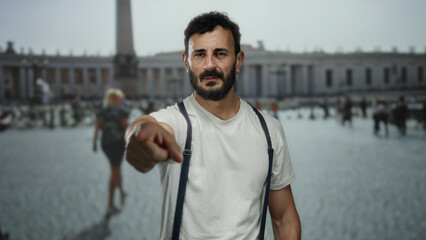 Fototapeta premium Hispanic man with beard wearing suspenders points in old town rome with blurred obelisk background capturing urban exploration mood.