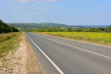 Scenic open road with sunflowers field and trees under blue sky