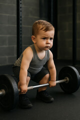 Determined toddler lifting a heavy barbell with serious focus in a gym setting