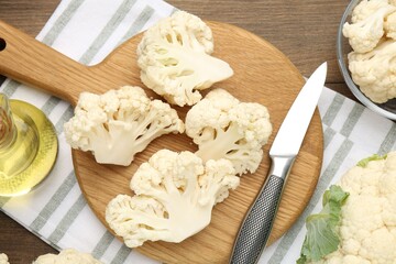 Fresh raw cauliflower florets, knife and oil on wooden table, flat lay