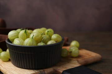 Fresh green gooseberries in bowl on wooden table, closeup. Space for text