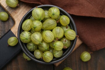 Fresh green gooseberries in bowl on wooden table, top view