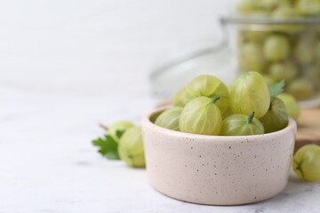 Fresh green gooseberries in bowl on white table, closeup. Space for text