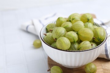 Fresh green gooseberries in bowl on white table, closeup