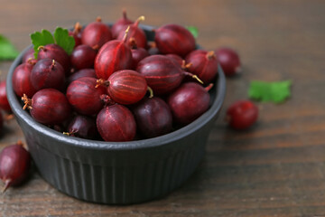 Ripe red gooseberries in bowl on wooden table, closeup