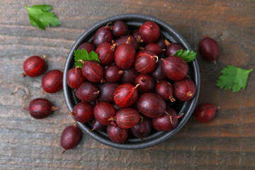 Ripe red gooseberries in bowl on wooden table, flat lay