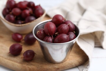 Ripe red gooseberries in bowl on white wooden table, closeup