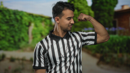 Young hispanic man referee flexing muscles with confidence in a vibrant outdoor park setting...