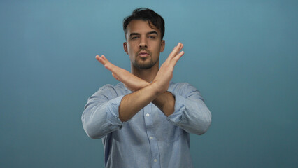 Young hispanic man isolated against blue background making a stop gesture with serious expression,...