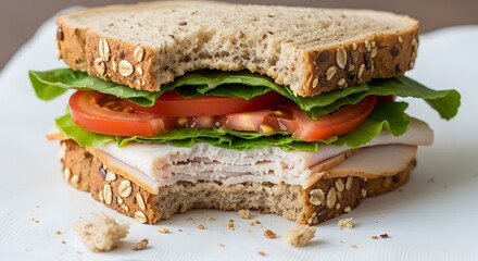 A partially eaten turkey sandwich with lettuce and tomato on multigrain bread on a white plate