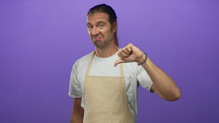 Blond man with long hair and apron displays thumbs down gesture in a purple studio setting;...