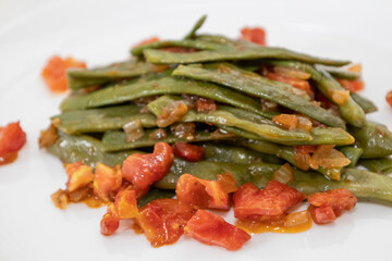 Fried green beans with tomato and onion pieces. Tasty meal with french bean on dinner or lunch on the white plate