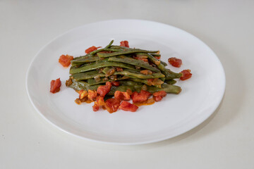 Fried green beans with tomato and onion pieces. Tasty meal with french bean on dinner or lunch on the white plate