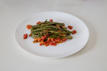 Fried green beans with tomato and onion pieces. Tasty meal with french bean on dinner or lunch on the white plate