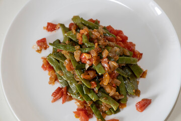 Fried green beans with tomato and onion pieces. Tasty meal with french bean on dinner or lunch on the white plate