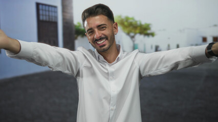 Man with white shirt and smartwatch extends bare hands towards camera in sunlit historic old town...